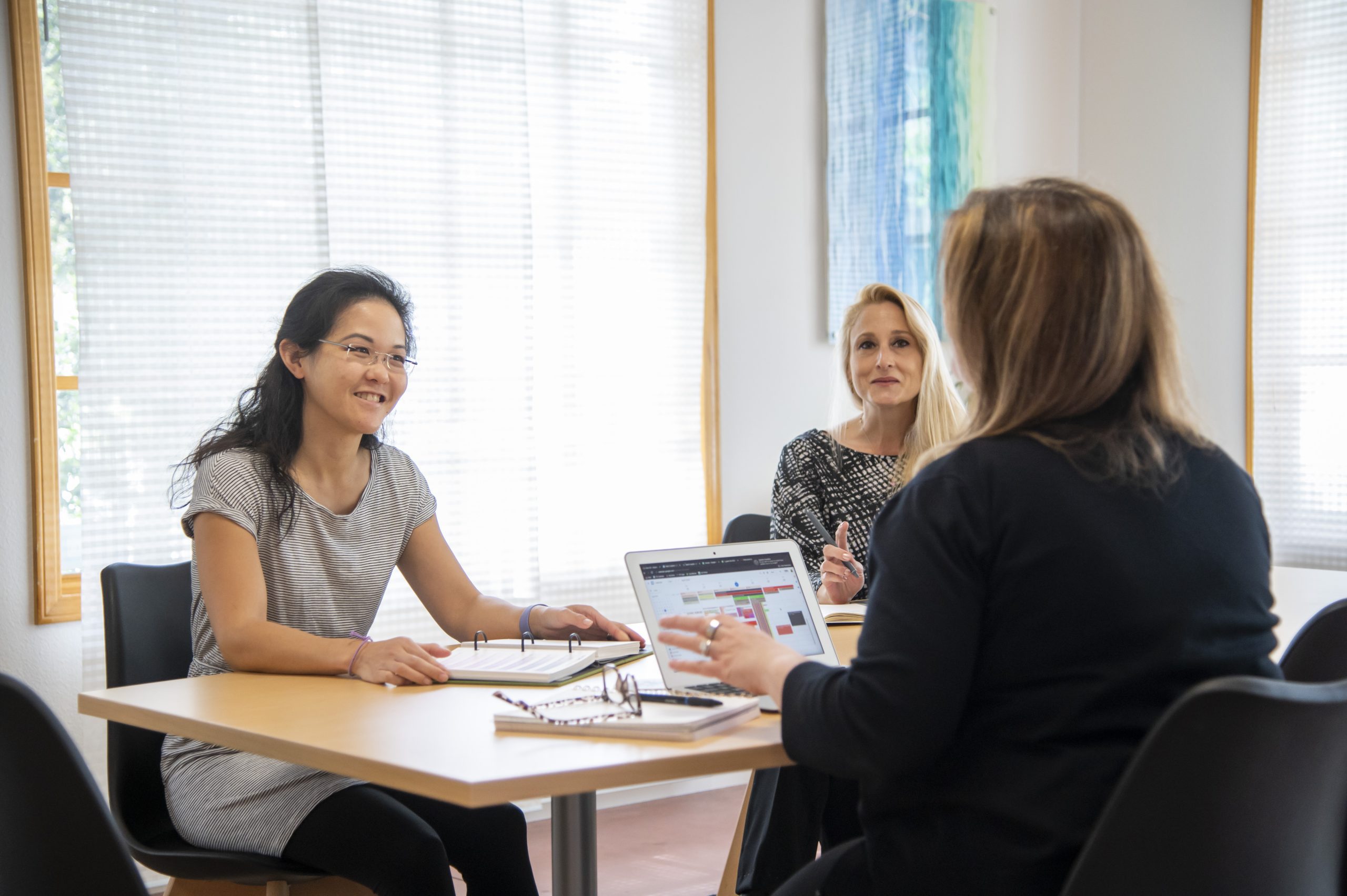 three people talking at a table with a laptop